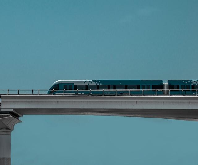 A modern train crossing an elevated bridge against a clear sky.